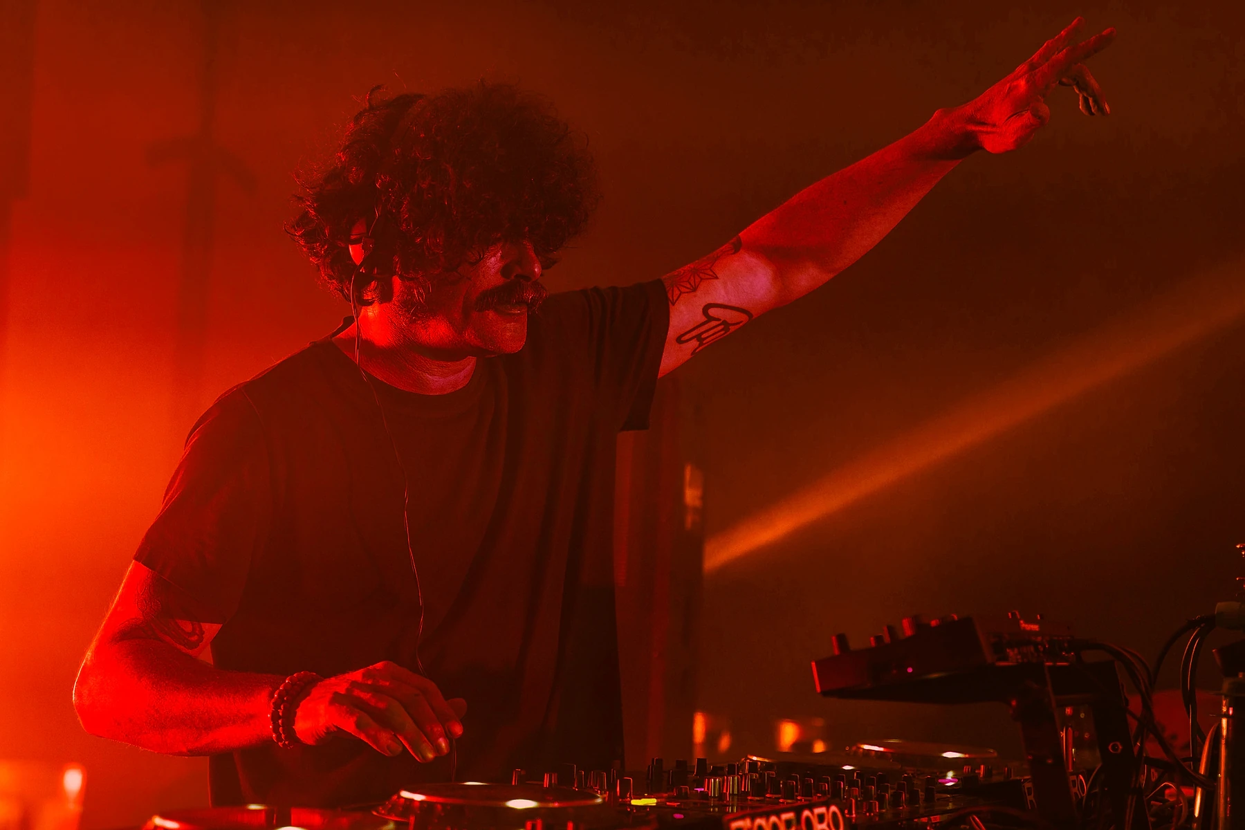 DJ con el brazo en alto sobre la cabina, iluminado en rojo
